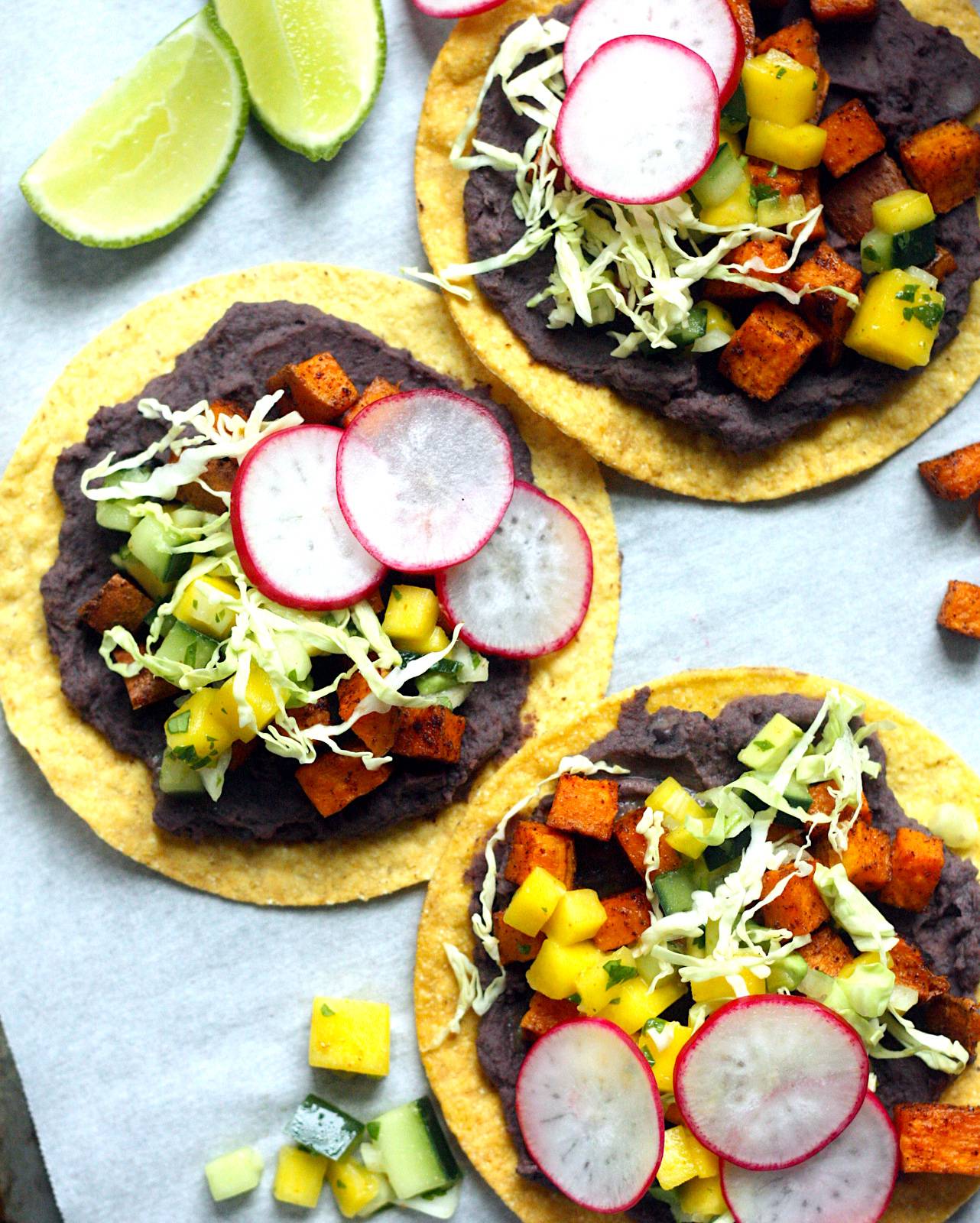 Tostadas topped with refried black beans, roasted sweet potatoes and mango salsa
